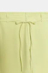 Pantalón blanco de tiro medio con pierna ancha y tejido que contiene lino. Presenta cintura con trabillas y un cinturón ajustable con lazada del mismo tejido. Cierre frontal con cremallera y botón.