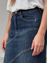 Pollera larga de denim con tiro alto, diseño ajustado en la parte superior y corte acampanado hacia el ruedo. Presenta costuras decorativas en diagonal que aportan movimiento y estructura a la prenda.