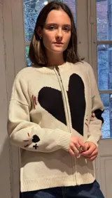 Campera tejida en hilo color crudo con diseño de corazón negro central, cierre frontal completo y detalles bordados en rojo y negro en mangas y cuerpo.