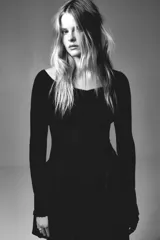 Top negro de manga larga, tejido en punto acanalado, con escote amplio tipo barco que deja los hombros al descubierto y un leve escote en V. El bajo y los puños terminan con un ribete fino de volados.