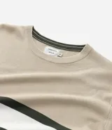 Suéter de punto con cuello redondo y manga larga, diseñado con un patrón de bloques de color en tonos beige, blanco y gris. Presenta un corte regular que se ajusta de forma anatómica al cuerpo.