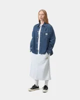 Camisa de denim azul de corte holgado, con cuello clásico, cierre frontal de botones metálicos y bolsillo parche en el pecho con etiqueta cuadrada de la marca.