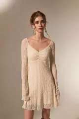 Vestido corto de encaje color crema, con mangas largas, cuello en V y falda evasé con terminación de volado.