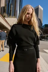 Vestido midi de punto en color negro, con cuello barco y mangas largas con sisa ancha. Presenta una cintura entallada con un cinturón fino incorporado con hebilla metálica dorada.