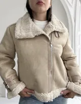 Chaqueta color beige con interior de piel sintética blanca, cierre cruzado con cremallera y detalles de hebillas en los puños.