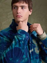 Sobrecamisa de tejido polar con estampado abstracto en tonos rojizos y azul marino. Presenta cuello clásico, cierre frontal con botones a presión, dos bolsillos frontales con solapa en el pecho y un parche decorativo.