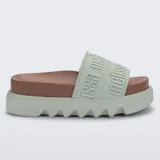 Sandalias plataforma Melissa modelo Cozy Slide M-Lover, color verde menta con plantilla marrón. Cuenta con una faja ancha superior con el nombre de la marca en relieve y suela chunky con relieve ondulado.
