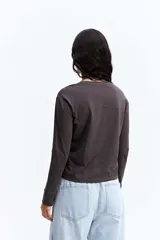 Remera de manga larga color gris oscuro, con cuello redondo y estampa gráfica frontal en tonos blancos y celestes con motivos florales y texto.