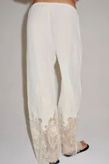 Pantalón de tiro medio con cintura elástica ajustable mediante cordones. Presenta un diseño fluido con bolsillos laterales ocultos y bajo decorado con una aplicación de encaje a contraste.