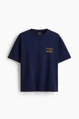 Remera azul marino de corte holgado con cuello redondo y estampado pequeño en el pecho con un avión y texto en color ocre.