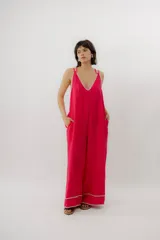 Mono enterito de lino color fucsia, con escote en V, tirantes dobles regulables, bolsillos laterales y detalles de costuras decorativas en contraste en el escote y los tobillos. Presenta una silueta amplia y relajada de pierna ancha.