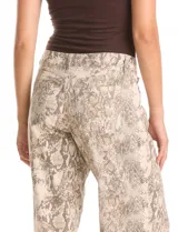 Jean de corte wide leg con estampado animal print de serpiente en tonos beige y gris. Presenta diseño clásico de cinco bolsillos, presillas para cinturón y cierre frontal con botón metálico.
