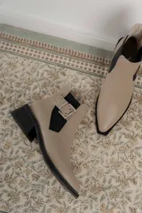 Botín negro de charol con punta cuadrada y hebilla metálica decorativa.