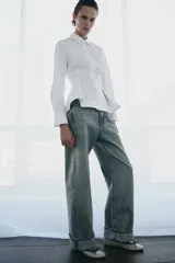 Camisa de popelín de algodón con cuello solapa, manga larga con puños y bajo con diseño peplum. Presenta cierre frontal oculto con botones.