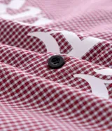 Camisa de corte oversized confeccionada en algodón, con estampado de cuadros tipo pied de poule en color rojo y blanco. Presenta cuello inglés, cierre frontal con botones y estampado lettering Breakout en el frente.