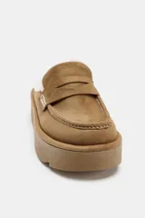 Mocasín destalonado de plataforma con acabado en gamuza color tostado. Presenta forro interior de efecto borreguito, detalle de antifaz en el empeine y pespuntes decorativos en contraste.