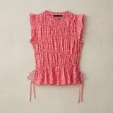 Musculosa sin mangas con estampado de cuadros vichy en tonos rojo y blanco, cuello redondo y diseño fruncido en el cuerpo. Cuenta con volados pequeños en los hombros y tiras ajustables con lazos en los laterales de la cintura.