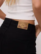 Falda de jean color negro, de corte recto y tiro medio, con ruedo deshilachado y cierre frontal con botón metálico.