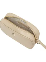 Cartera tipo camera bag de Tommy Hilfiger en color beige, con acabado liso y cierre de cremallera. Presenta el monograma TH metálico en la parte frontal y cuenta con una correa ajustable y extraíble.