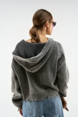 Campera con capucha de tejido de punto acanalado en color gris oscuro con efecto lavado. Presenta cierre frontal completo con tirador circular, bolsillos tipo canguro y logo bordado en relieve en el pecho. Posee terminaciones con bordes deshilachados en puños y ruedo.