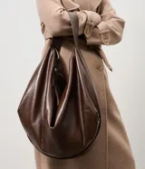 Cartera modelo hobo de gran tamaño, confeccionada en poliuretano con acabado brillante y textura suave. Presenta un diseño de media luna con asa ancha integrada para llevar al hombro y cierre superior.