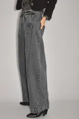Jean de corte wide leg en color gris oscuro con efecto lavado. Presenta costuras verticales decorativas a lo largo de las piernas y cierre frontal con botón y cremallera.