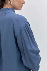 Camisa azul de manga larga con cuello alto fruncido y puños elásticos.