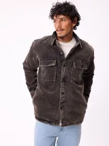 Sobrecamisa de pana color marrón oscuro con efecto desgastado, cierre frontal con botones, dos bolsillos frontales con solapa y forro interior acolchado.