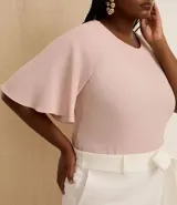 Blusa de crepé color rosa pálido, con cuello redondo, mangas cortas con volados, lazo en la cintura y botón en la espalda.