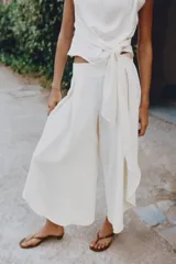 Pantalón fluido de tiro alto en color blanco, con pinzas delanteras, cintura elástica en la espalda y perneras anchas con aberturas laterales pronunciadas.