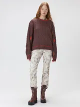 Sweater de punto con diseño de ochos en color verde, cuello redondo con detalle de franja en contraste, y apliques de rombos en las mangas. Presenta un bordado con la letra M en el pecho.