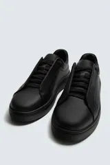 Zapatilla negra de cordones, con parte superior lisa y cordonera oculta. Posee suela con volumen a tono.