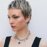 Par de aros colgantes plateados con forma de cruz ornamentada y cierre tipo argolla.