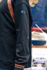 Buzo amarillo de corte holgado con mangas raglán en color azul, detalle de costuras acolchadas en los hombros y bordado de sol en el centro del pecho. Presenta puños y cuello acanalados con rayas azules.