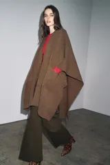 Capa de punto color marrón, con escote en V, mangas cortas y bolsillos de plastrón en el delantero. El ruedo tiene un corte asimétrico.