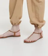 Sandalia plana de mujer color dorado metalizado, con diseño minimalista de tira fina que une la puntera y el empeine, y tira elástica fina alrededor del tobillo.