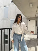 Blusa cruzada color blanco con lazo para anudar en la cintura, cuello camisero y mangas largas amplias.