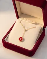 Collar estilo corbatero de plata con baño de oro, presenta un punto de luz central y un dije circular con esmalte rojo rodeado de pequeñas piedras brillantes.