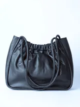Bolso tipo tote bag de cuero negro, con diseño fruncido en la parte superior y dos asas delgadas de hombro. Presenta un acabado de cuero suave y arrugado.