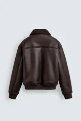 Cazadora oversize de efecto piel color negro, con interior y cuello solapa de pelo sintético gris a contraste. Cuenta con bolsillos de vivo en la cadera, acabados en rib elástico y cierre frontal con cremallera.