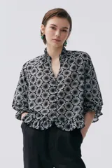 Blusa negra con estampado de flores blancas, escote en V con volados, mangas 3/4 abullonadas con elástico y botones forrados.