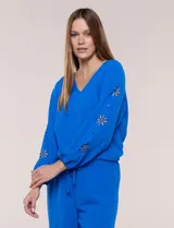 Blusa azul de corte holgado y fluido, con escote en V y mangas largas raglán que presentan detalles de calados con forma de flores y puños elastizados.