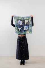 Pañuelo cuadrado de seda con estampado floral y geométrico en tonos azules, verdes y blancos sobre fondo negro.