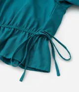 Blusa color verde azulado con escote bardot, mangas cortas abullonadas con elástico y cintura con lazo ajustable.