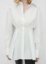 Camisa de algodón con cuello camisero, diseño largo y entallado con pliegues frontales. Presenta cierre delantero de botones ocultos y mangas largas con detalle metálico en los puños.