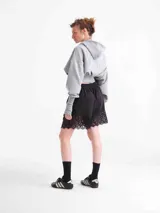 Campera negra de tela deportiva fina con capucha, cierre frontal completo, diseño estilo corset en la cintura y mangas largas con puños tipo guante con abertura para el pulgar.