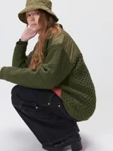 Campera tejido grueso y abrigado color verde militar, con forro de nylon interno, cuello estilo camisa en color negro y cierre frontal con botones. Cuenta con cuatro bolsillos delanteros con apliques en distintos tonos y texturas, y un parche bordado circular en el bolsillo superior izquierdo.