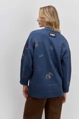 Cardigan de punto azul con cuello en V, cierre frontal de botones y bolsillos delanteros. Presenta bordados decorativos con motivos variados y frases en colores contrastantes.