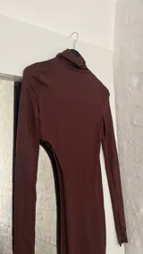 Top marrón de cuello alto y manga larga, con abertura en el abdomen y falda asimétrica.