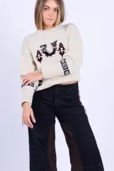 Sweater de punto tejido a dos agujas en lana merino, color crudo con detalles bordados en azul marino y vino. Presenta un corte boxy, cuello redondo y puños con elástico ancho.